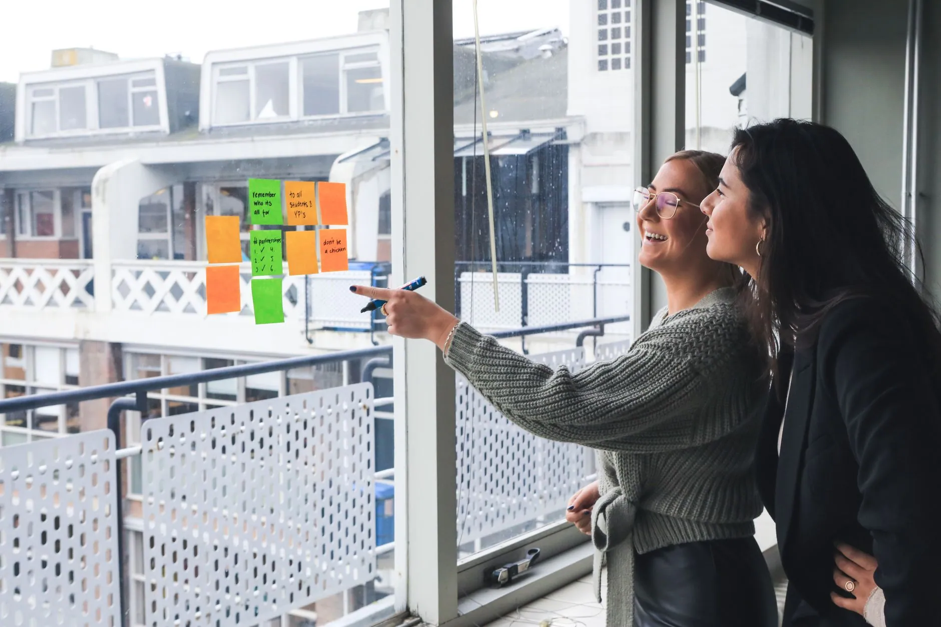Two colleagues planning with sticky notes by a window